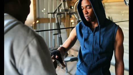 Afroamerikanischer-Männlicher-Trainer-Unterstützt-Boxer-Beim-Tragen-Von-Handwickel-Im-Fitnessstudio-4k