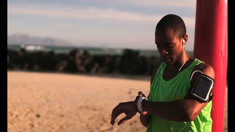 African-American-male-jogger-using-smartwatch-on-beach-in-the-sunshine-4k