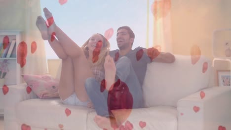 Happy-couple-jumping-on-the-sofa-with-digital-hearts-on-the-foreground