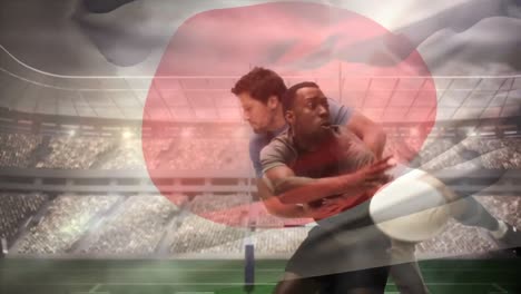 Rugby-player-throwing-ball-while-being-tackled-down-by-player-and-Japanese-flag-waving-in-full-stadi
