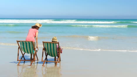 Rückansicht-Eines-Aktiven-älteren-Afroamerikanischen-Paares-Mit-Hut,-Das-Sich-Auf-Einem-Liegestuhl-Am-Strand-Entspannt,-4k