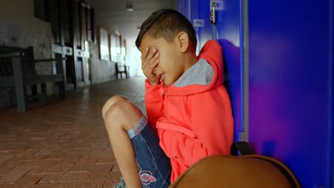 Side-view-of-Asian-schoolboy-sitting-alone-with-hands-covering-his-face-in-school-corridor-4k