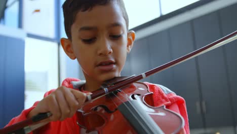Front-view-of-attentive-Asian-schoolboy-playing-violin-in-classroom-at-school-4k