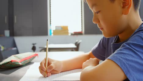 Side-view-of-attentive-Asian-schoolboy-studying-at-desk-in-classroom-at-school-4k
