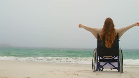 Side-view-of-young-Caucasian-woman-sitting-with-arms-outstretched-on-wheelchair-at-beach-4kouple-hav