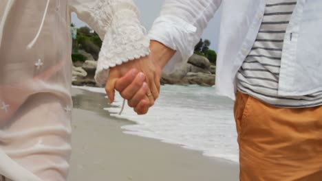 Mid-section-of-couple-walking-hand-in-hand-on-the-beach-4k