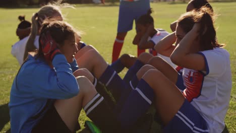 Female-soccer-players-doing-sit-up-exercises-while-captain-gives-training-on-soccer-field.-4k