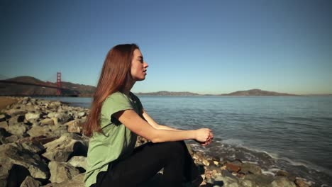 Woman-sitting-on-rocks-beside-the-Golden-Gate-Bridge