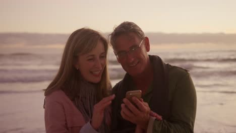 Active-senior-couple-using-phone-on-beach