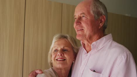 Senior-couple-in-social-distancing-hugging-each-other-in-retirement-house