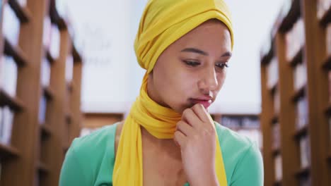 Asian-female-student-wearing-a-yellow-hijab-sitting-with-an-open-book-and-using-laptop