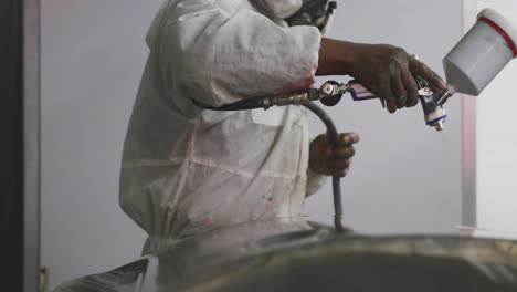 African-American-male-car-mechanic-with-a-suit-and-painting-a-piece-of-a-car-with-a-spraying-gun-