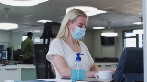 Woman-wearing-face-mask-using-computer-at-office