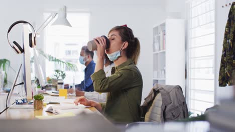Woman-drinking-coffee-while-sitting-on-her-desk-at-office