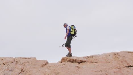 Senior-hiker-man-with-backpack-and-trekking-poles-walking-on-the-rocks
