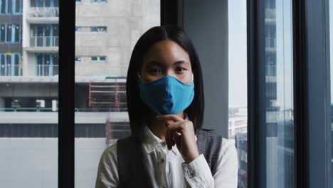 Porträt-Einer-Asiatischen-Frau-Mit-Gesichtsmaske,-Die-Im-Modernen-Büro-Steht