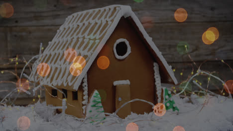 Animation-of-spots-of-light-over-gingerbread-house-in-snow