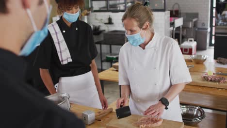 Caucasian-female-chef-teaching-diverse-group-wearing-face-masks