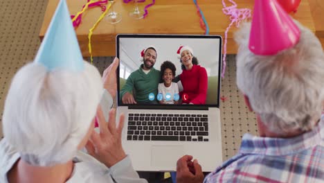 Kaukasisches-älteres-Paar-Mit-Partyhüten-Auf-Laptop-Videochat-Während-Weihnachten-Zu-Hause