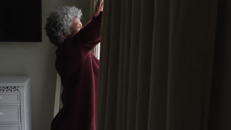 Senior-african-american-woman-opening-curtains-of-the-window-at-home
