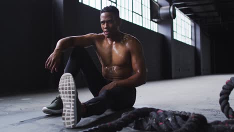 Shirtless-african-american-man-resting-after-battling-ropes-in-an-empty-urban-building
