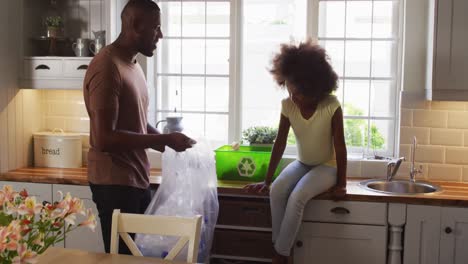 African-american-daughter-and-her-father-sorting-recycling-and-high-fiving-in-kitchen