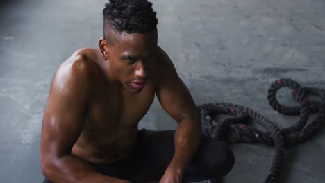 Shirtless-african-american-man-resting-after-battling-ropes-in-an-empty-urban-building