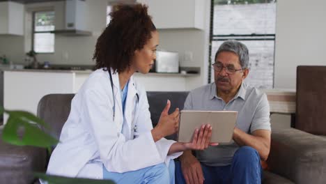 Mixed-race-female-doctor-and-senior-man-using-tablet-and-talking