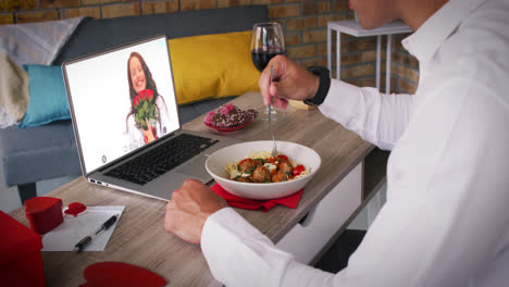 Kaukasisches-Paar-Bei-Einem-Valentinstag-Videoanruf,-Mann-Isst-Essen-Mit-Lächelnder-Frau-Auf-Laptop-Bildschirm