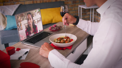 Diverse-couple-on-a-valentines-date-video-call-man-eating-meal-with-smiling-woman-on-laptop-screen