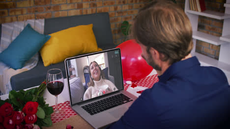 Caucasian-couple-on-a-valentines-date-video-call-man-waving-to-smiling-woman-waving-back-on-laptop-s