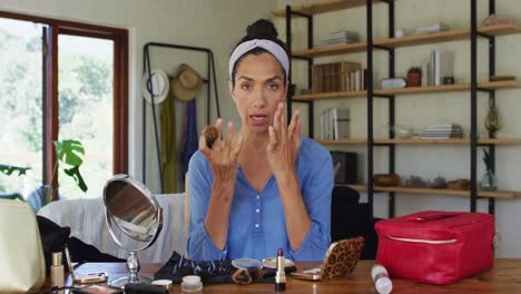 Portrait-of-mixed-race-female-vlogger-applying-make-up-at-home