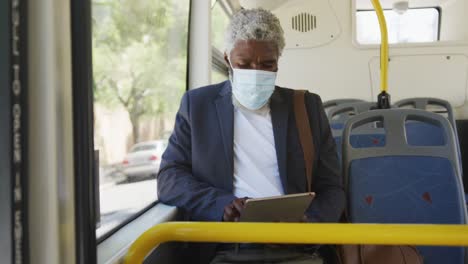 Afroamerikanischer-älterer-Mann-Mit-Gesichtsmaske-Und-Digitalem-Tablet,-Während-Er-Im-Bus-Sitzt