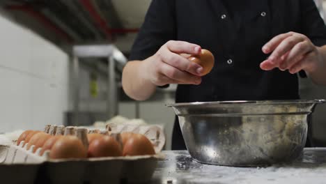 Midsection-of-caucasian-female-chef-breaking-eggs-into-metal-bowl