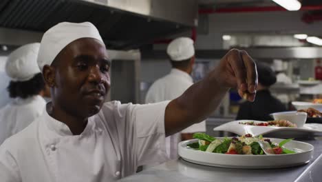 African-american-male-chef-garnishing-dish-and-similing-in-restaurant-kitchen