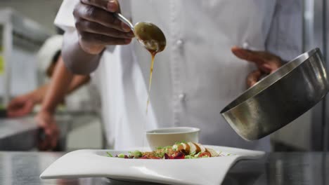 Midsection-of-african-american-frmale-chef-garnishing-dish-in-restaurant-kitchen