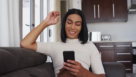 Mann-Mit-Fließendem-Geschlecht-Lächelt,-Während-Er-Zu-Hause-Auf-Der-Couch-Sitzt-Und-Sein-Smartphone-Benutzt