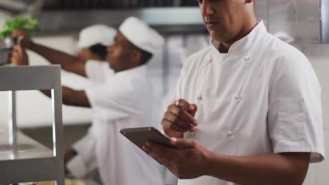 Mixed-race-male-chef-using-tablet-in-restaurant-kitchen