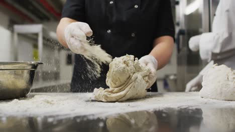 Midsection-of-caucasian-female-chef-wearing-rubber-gloves-and-preparing-dough