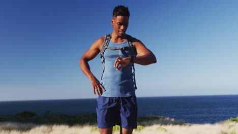 African-american-man-cross-country-running-using-a-smartwatch-in-countryside-on-a-mountain