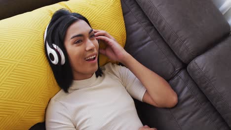 Gender-fluid-male-wearing-headphones-enjoying-listening-to-music-while-lying-on-the-couch-at-home