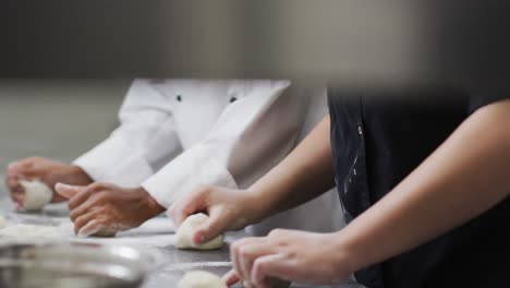 Two-diverse-female-chefs-preparing-dough-and-talking-in-restaurant-kitchen