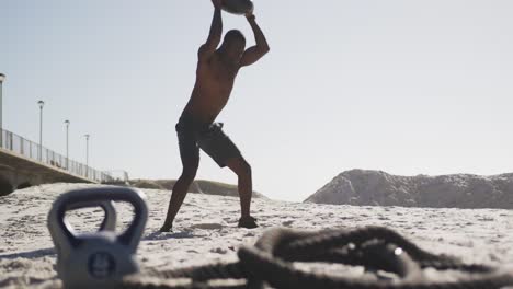 Afroamerikanischer-Mann,-Der-Am-Strand-Mit-Einem-Medizinball-Trainiert