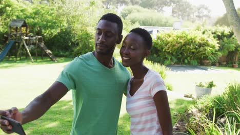Lächelndes-Afroamerikanisches-Paar,-Das-Ein-Selfie-Mit-Dem-Smartphone-Macht-Und-Sich-Im-Sonnigen-Garten-Umarmt