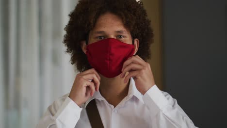 Portrait-of-mixed-race-man-with-curly-hair-putting-on-red-face-mask