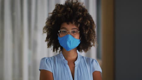 Portrait-of-mixed-race-woman-with-curly-hair-wearing-blue-face-mask