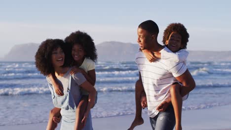 Afroamerikanische-Mutter-Und-Vater-Fahren-Huckepack-Mit-Ihrer-Tochter-Und-Ihrem-Sohn-Am-Strand