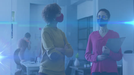 Animation-of-glowing-light-trails-over-women-in-office-talking-and-wearing-face-masks
