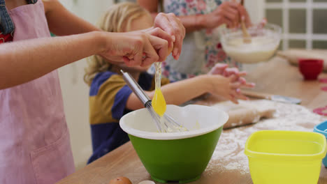 Midsection-of-caucasian-mother-in-kitchen-baking-son-and-daughter-breaking-egg-into-a-bowl