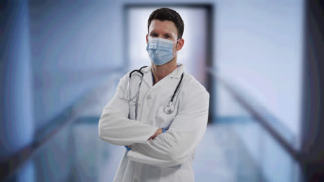 Caucasian-male-doctor-wearing-face-mask-standing-with-arms-crossed